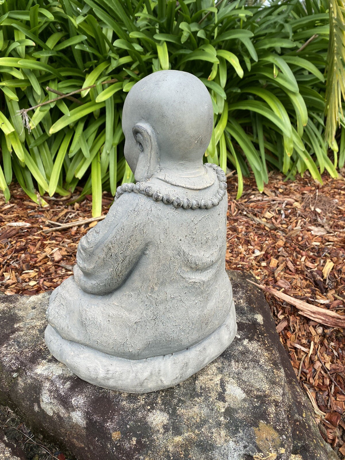 22nice4me Garden Statues Buddha figurine in GRC concrete with an antique finish, viewed from the back in a garden.