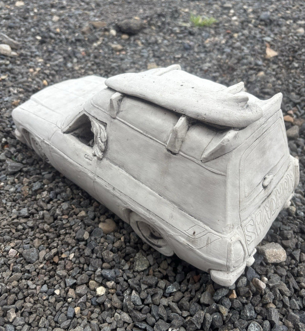 22nice4me Garden Statues concrete Sandman panel van ornament with roof surfboard on a gravel surface