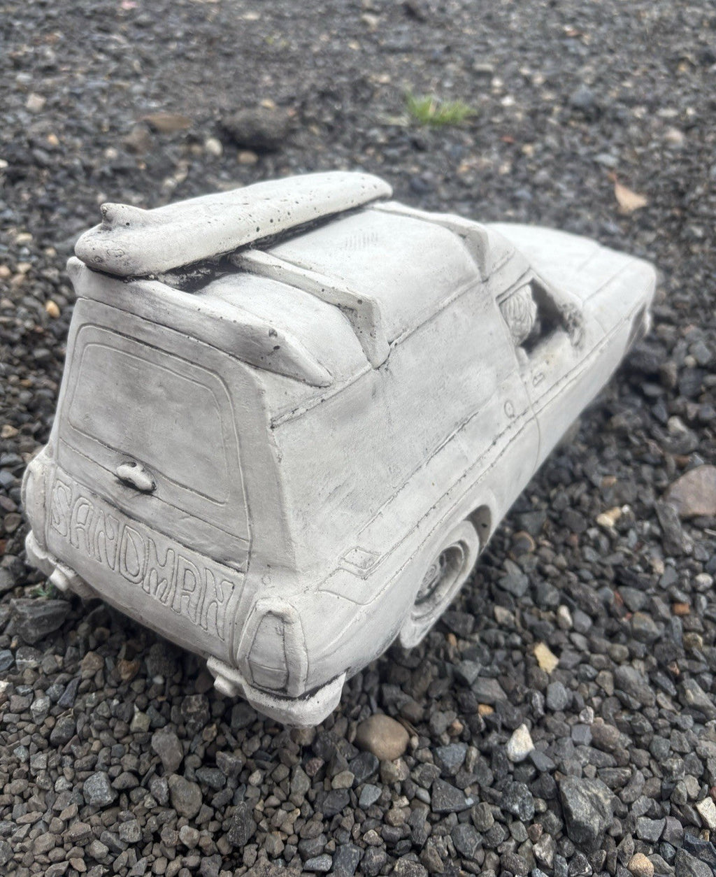 22nice4me Garden Statues concrete Sandman panel van ornament with a roof surfboard on a gravel surface