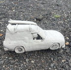 22nice4me Garden Statues concrete Sandman panel van ornament with a roof-mounted surfboard on a gravel surface