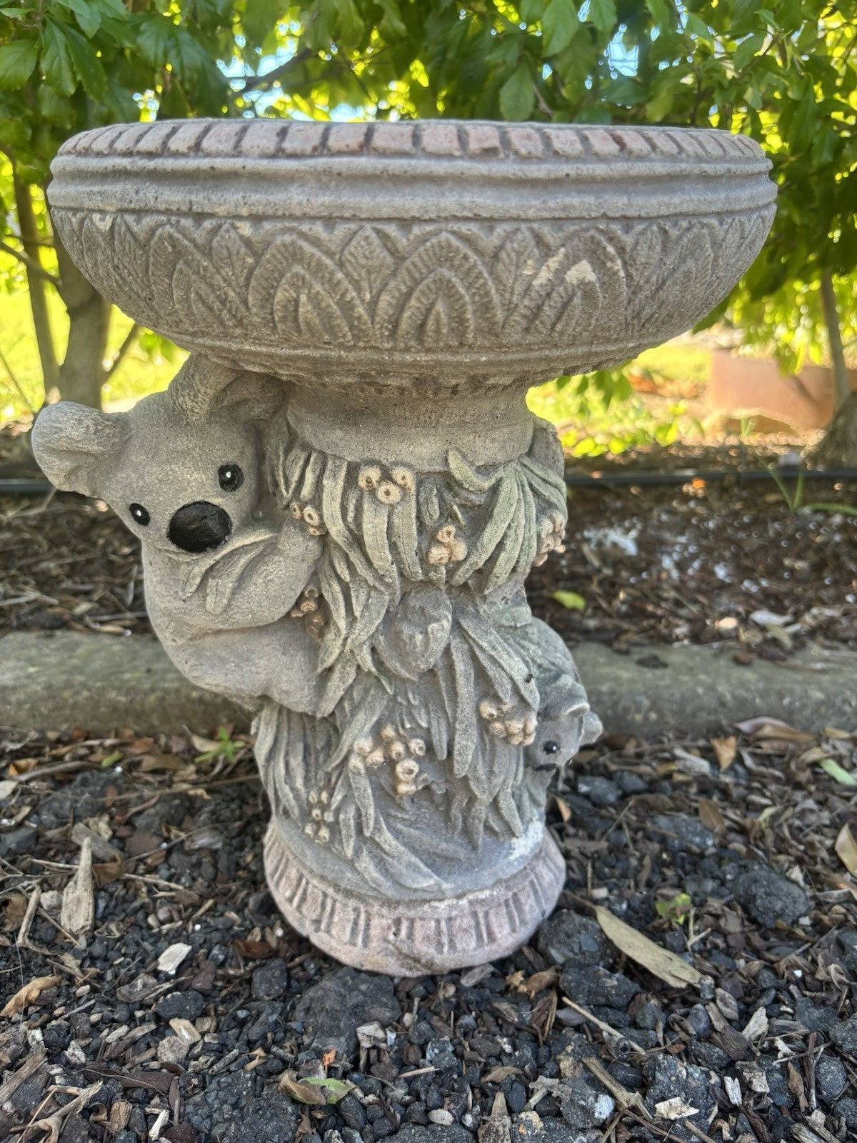 concrete bird bath featuring a sculpted koala and gum leaves in a garden setting